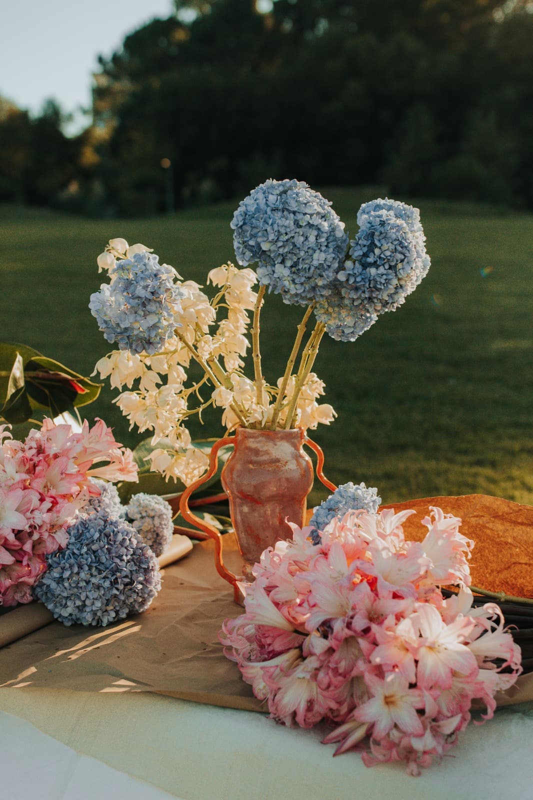 Outdoor tablescape at golden hour with blue hydrangea and pale florals in a terracotta vase